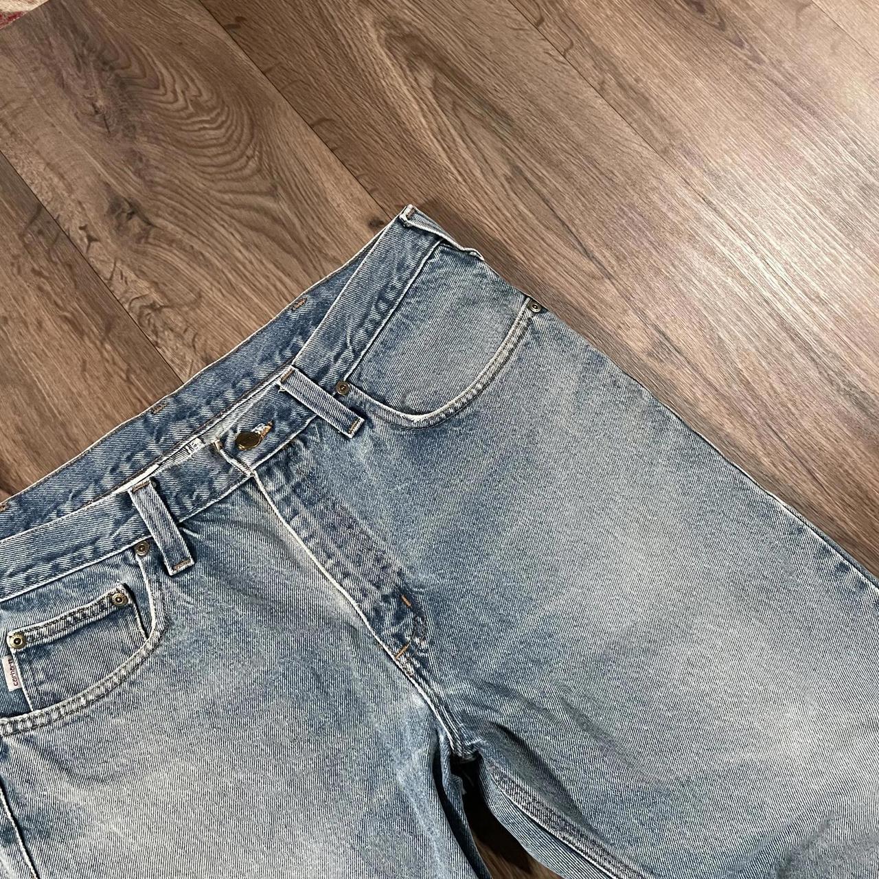The Madams Vintage Carhartt Blue Denim Jeans W36 L30 rest on a wooden floor. They showcase a classic five-pocket design with visible stitching and a button closure, capturing timeless workwear style.
