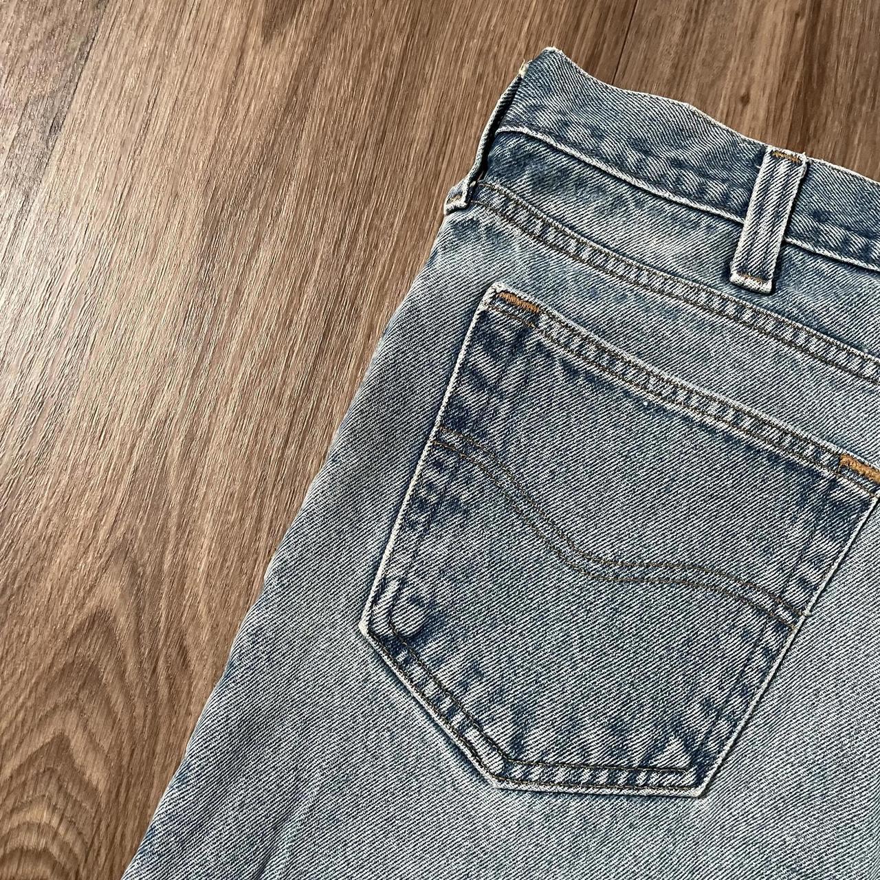 Close-up of the back pocket on Madams Vintage Carhartt Blue Denim Jeans W36 L30, showcasing visible stitching and slight texture. Positioned diagonally on a wooden floor, the pocket reveals part of the waistband and belt loop, exuding a classic workwear vibe with timeless style.