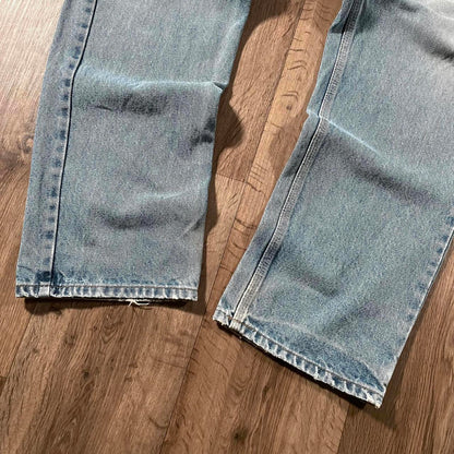 Close-up of Madams Vintage Carhartt Blue Denim Jeans W36 L30 on a wooden floor, featuring slightly faded legs, natural creases, and visible fringed hems.