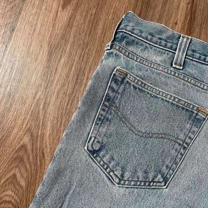 Close-up of the back pocket on Madams Vintage Carhartt Blue Denim Jeans W36 L30, showcasing visible stitching and slight texture. Positioned diagonally on a wooden floor, the pocket reveals part of the waistband and belt loop, exuding a classic workwear vibe with timeless style.